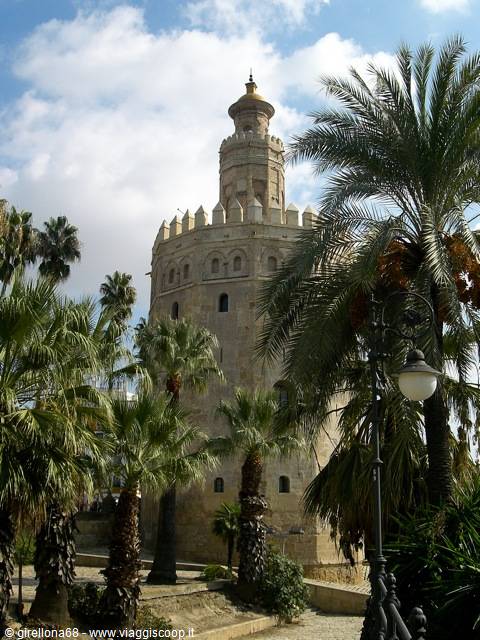 Torre del Oro in Seville, golden tower surrounded by palm trees under white clouds