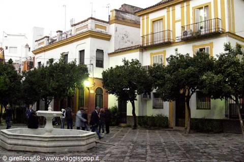 Small square with stone fountain among orange trees and yellow Andalusian houses