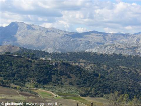 Rocky mountains above green hills with scattered houses, white clouds in the sky