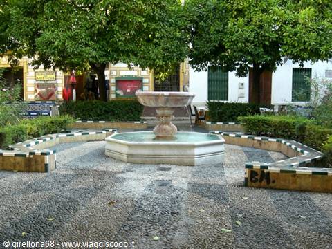 Marble fountain in the center of a tree-lined square with tiled planters