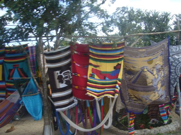 Colorful woven blankets and hammocks hanging under a tree at outdoor craft market
