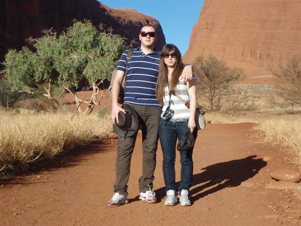 Couple with camera on red sand path between Uluru rock formations