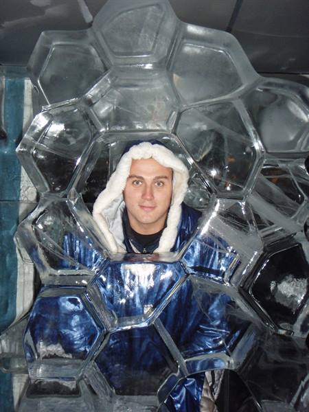 Hooded man peers through a hole in an hexagonal ice sculpture