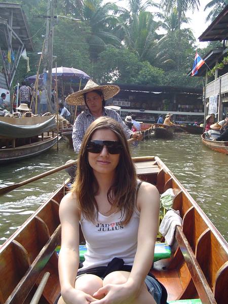 Tourist on a wooden boat at a floating market, a vendor in straw hat rows