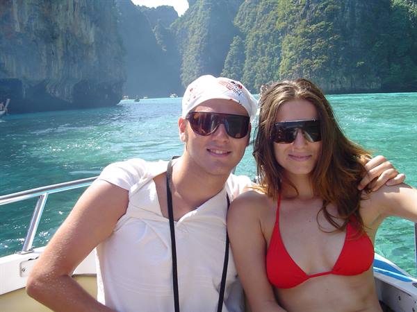 Couple in sunglasses on a boat among green cliffs and turquoise water, Maya Bay