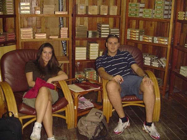 Two young people in wicker armchairs among wooden shelves of cigar boxes