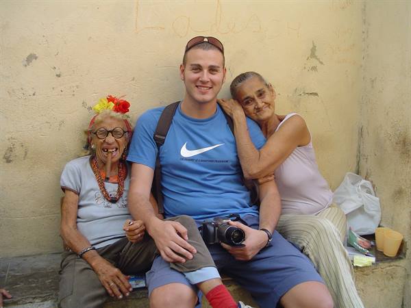 Smiling tourist with two elderly women, camera in hand, yellow wall