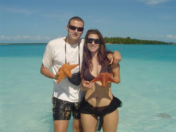 Couple in sunglasses standing in turquoise water holding orange starfish