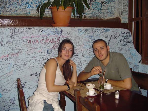 Couple at La Bodeguita del Medio table, signature-covered wall, coffee and mojito