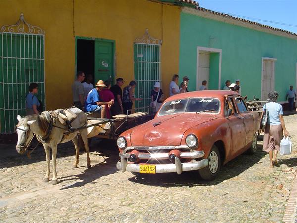 Rusty red Ford car and horse cart on cobblestone street beside colorful colonial houses