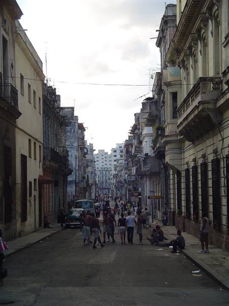 Potholed street lined with weathered colonial buildings, pedestrians walking, Havana