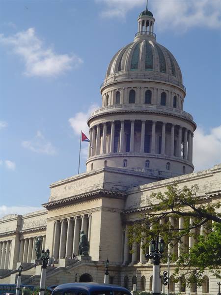 Stone dome of Havana's Capitolio, Cuban flag, daylight, vintage car below