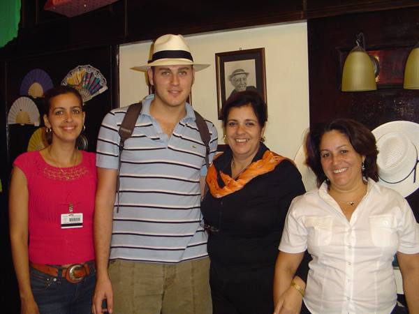 Four smiling people in a straw hat shop, warm indoor lighting
