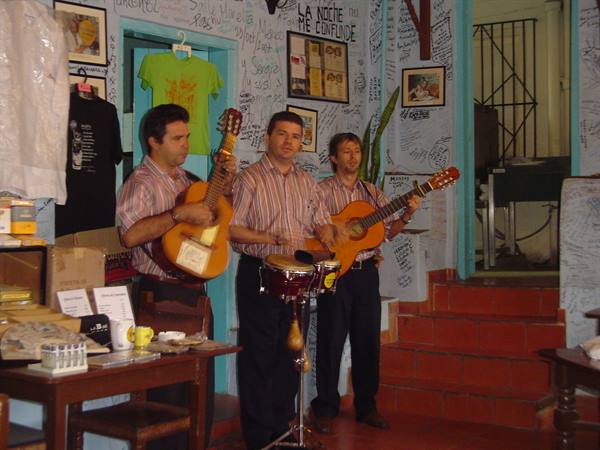 Three musicians playing guitars and bongos in a signature-covered bar, Havana