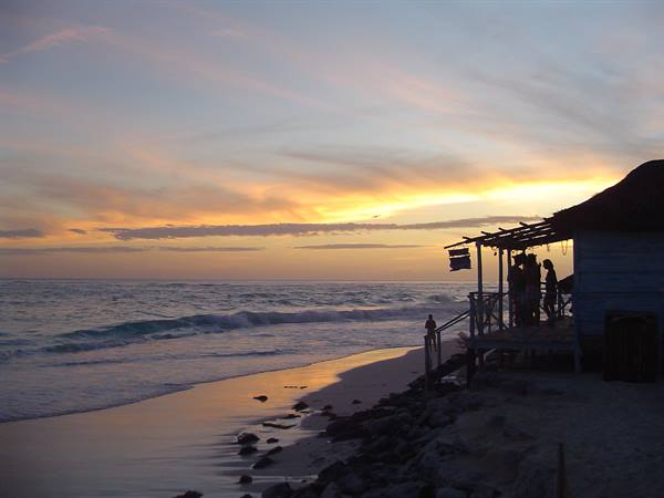 People on the wooden veranda of a beach hut at dusk