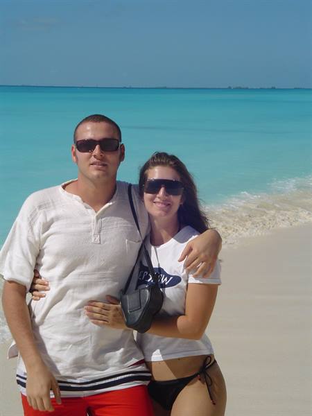 Couple in sunglasses hugging on white sand beach in front of turquoise sea