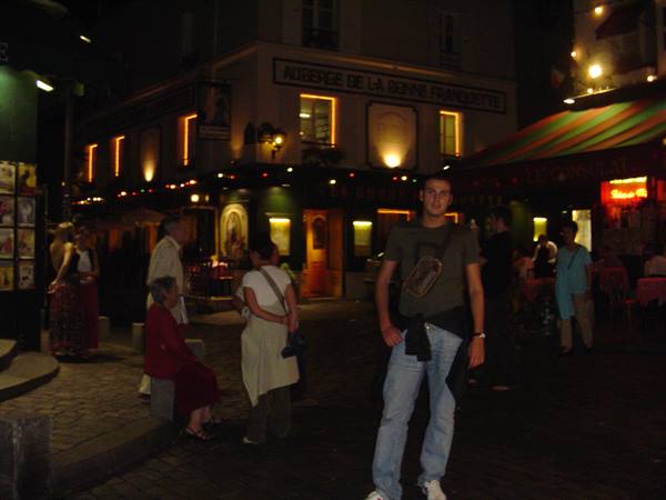Young man in jeans outside lit cafés on Place du Tertre, Montmartre