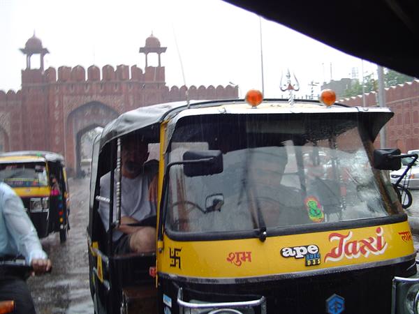 Yellow Ape taxi rickshaw in the rain before a red sandstone gate, Jaipur