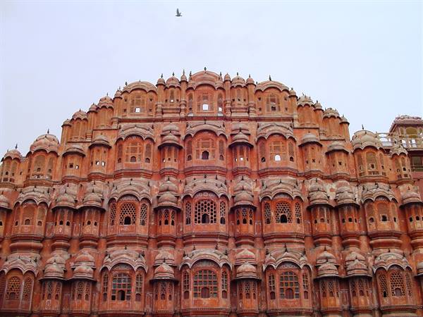 Hawa Mahal in Jaipur, red sandstone facade with arched windows, bird flying above