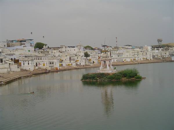 Pushkar sacred lake with marble ghats and white buildings under grey sky