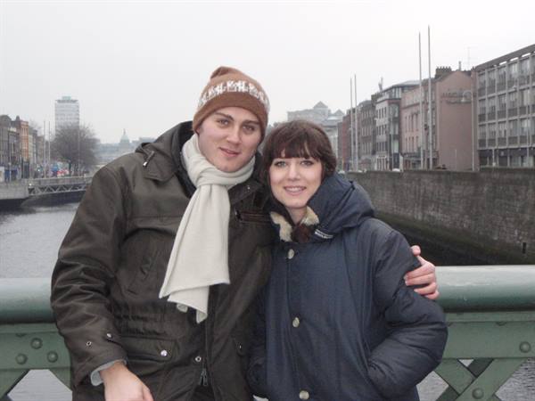 Couple hugging on a green bridge over the river, coats and scarf