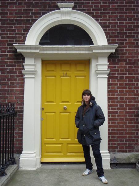 Woman posing by a yellow Georgian door on a red brick facade