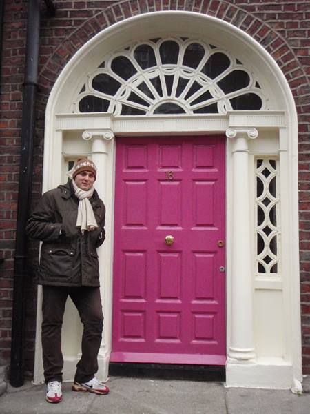 Man with scarf beside pink Georgian door with white fanlight on red bricks