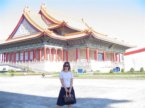 Woman in front of temple with golden roof and red columns, bright light