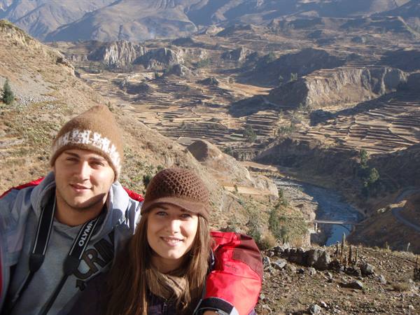 Two smiling travelers in front of Colca's farming terraces and river