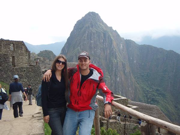 Smiling couple in red jacket beside the stone ruins of Machu Picchu