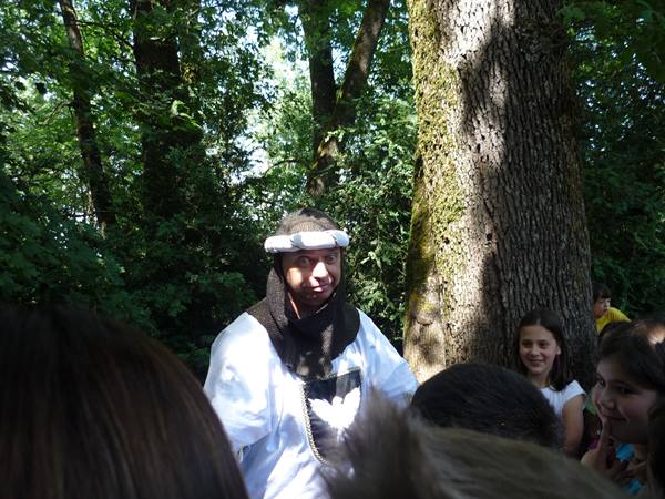 Man in white medieval costume talks to children under the trees
