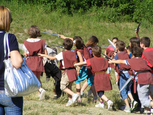 Children in brown tunics with wooden swords playing on a sunny meadow