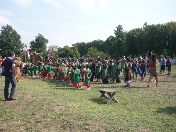 Children in green and red costumes with shields at medieval reenactment in park