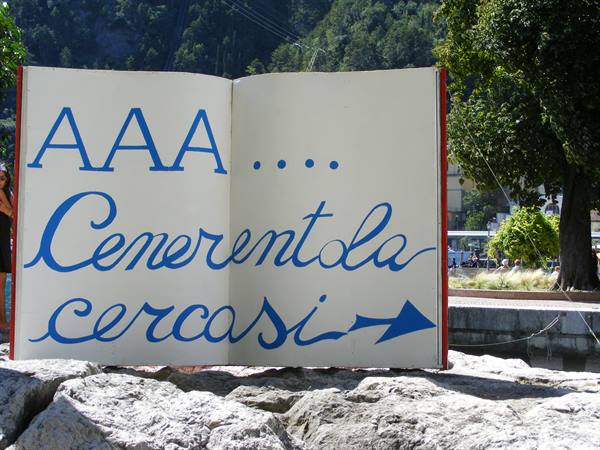 Open book sculpture reading AAA Cenerentola cercasi, among rocks and trees