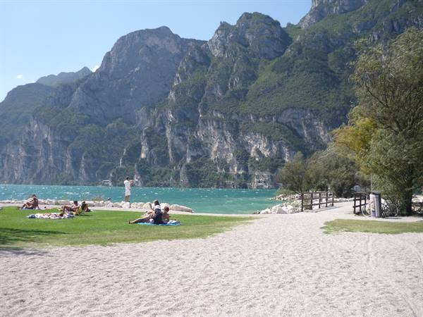 Sandy beach on Lake Garda, people sunbathing beneath rocky cliffs