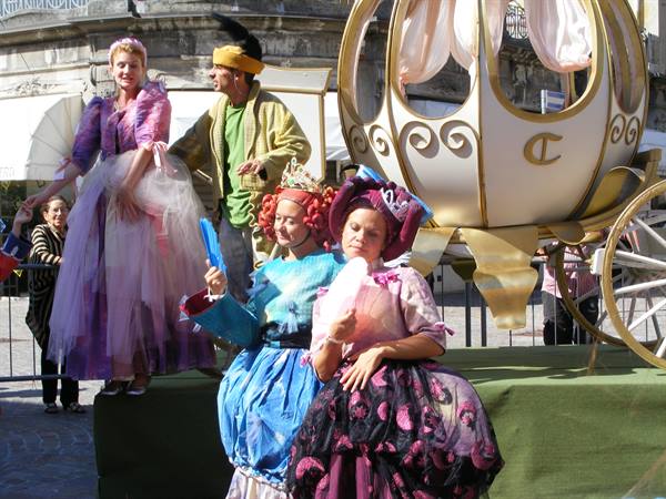Actors in theatrical costumes beside a golden carriage in a square