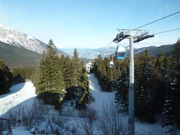 Cable car above snowy ski slopes among fir trees and mountains