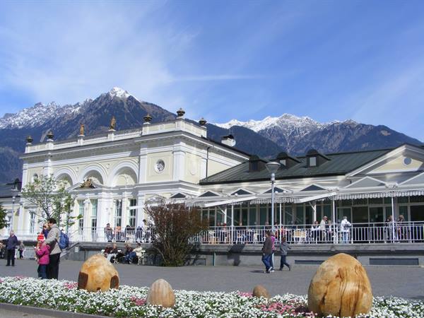 People strolling in front of the Kurhaus Merano under snowy Alps