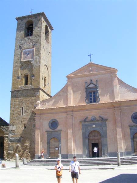 Tourists walk in front of a pink church facade with medieval bell tower
