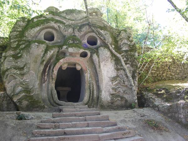 Giant mossy stone Orcus head with dark mouth entrance and steps, Bomarzo
