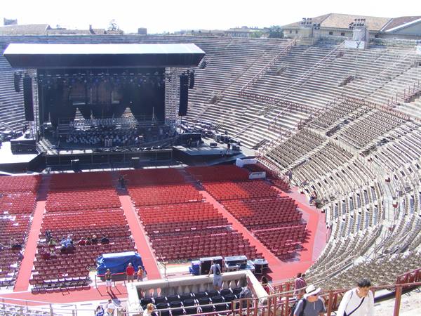 Verona Arena: stage and red chairs inside the stone amphitheater, workers setting up
