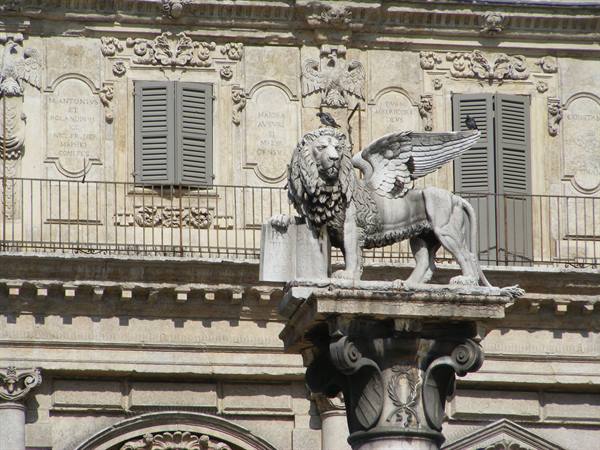 Winged lion statue of Saint Mark on a column before a marble palace