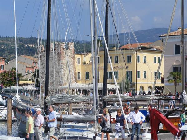 Tourists stroll among moored sailboat masts at the Bardolino harbor