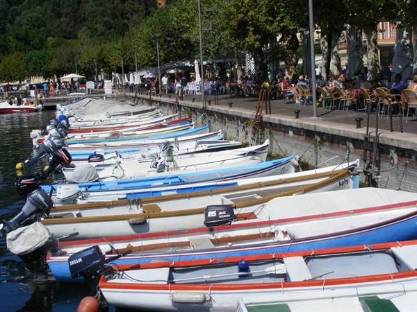 Motorboats moored along Bellagio waterfront, people seated at outdoor cafés