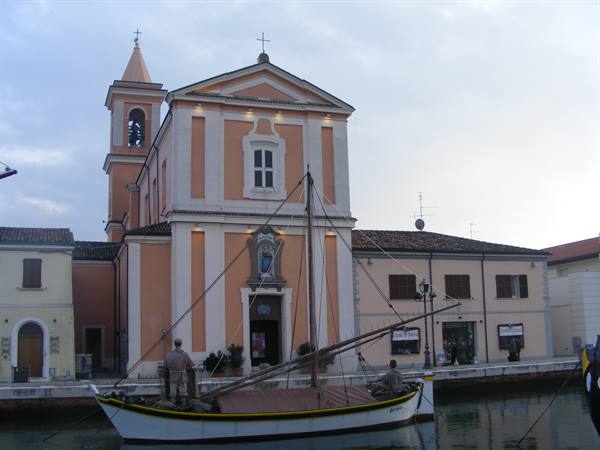 Pink church with bell tower by the canal, sailboat moored at the dock