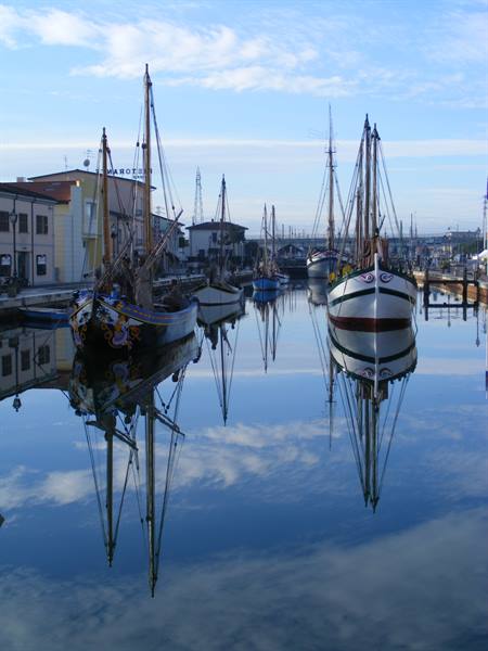 Historic sailing boats moored along Cesenatico canal harbor, mirrored in calm water