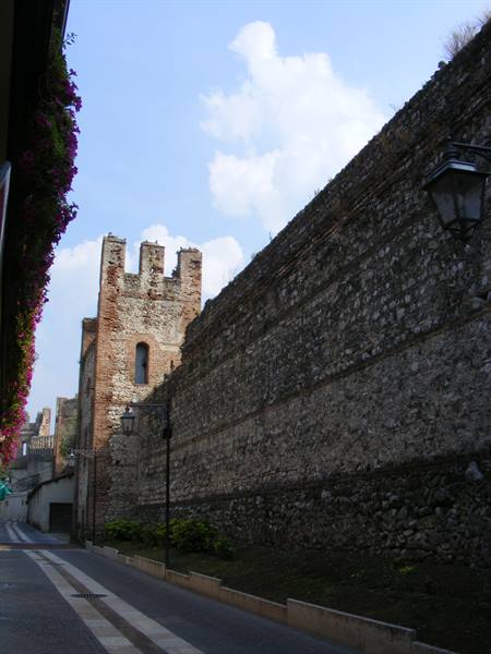 Ancient stone city wall with crenellated tower beside a quiet street