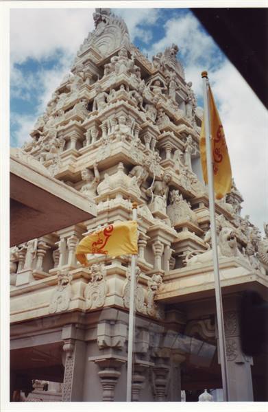 White carved gopuram tower with statues under cloudy sky, yellow flags flying