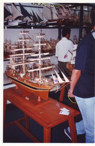Wooden model of a multi-masted sailing ship on table, visitors among shelves of boats