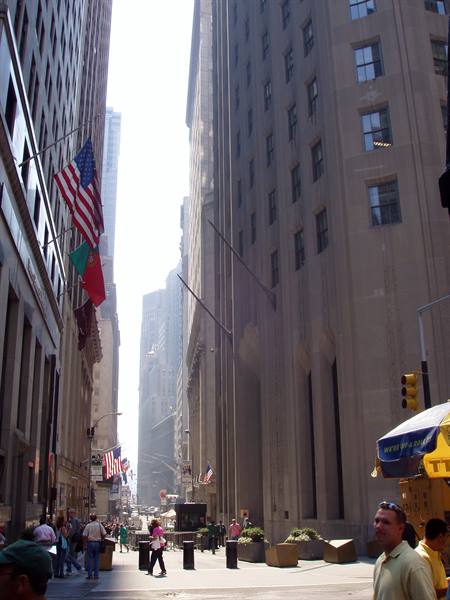 American flags on Wall Street skyscrapers, pedestrians walking in morning light
